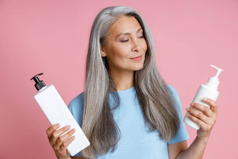 woman standing in front of a pink background holding bottles of shampoo