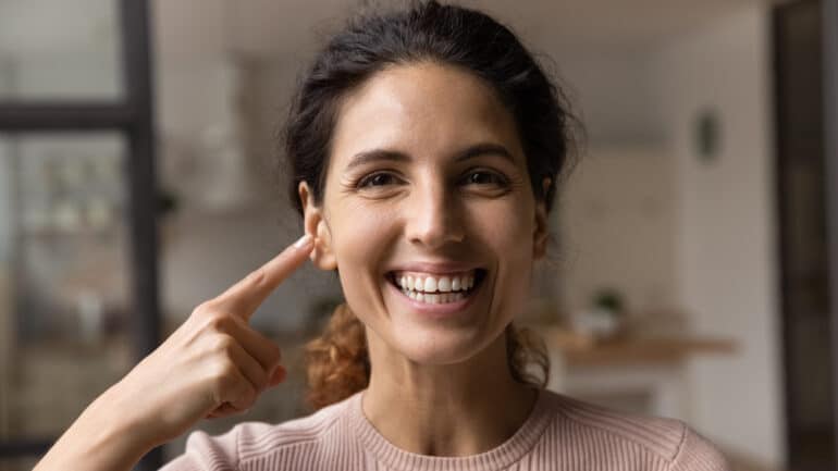 Hispanic woman smiling and pointing at the clear skin on her face