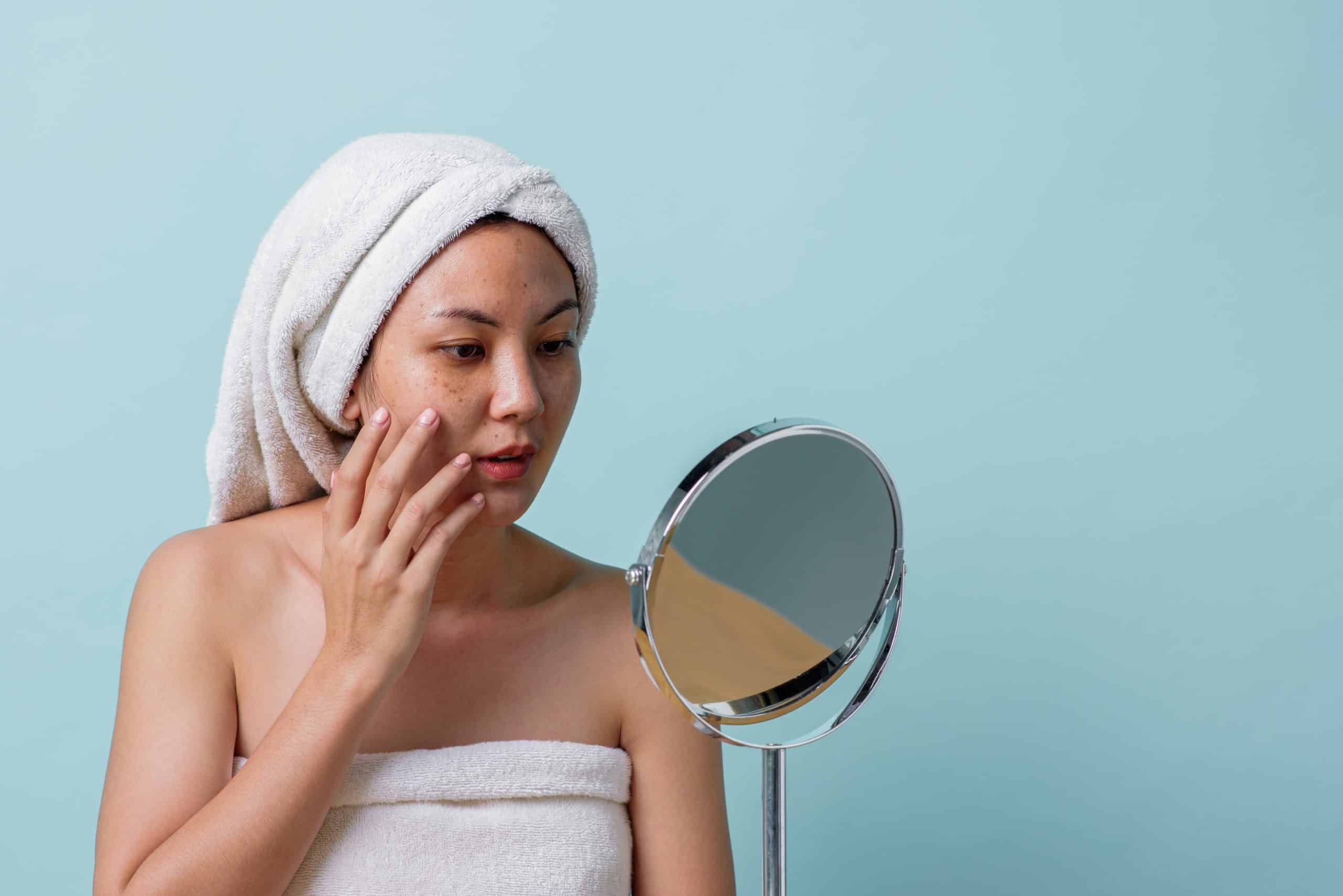 woman looking at her dark spots in a mirror