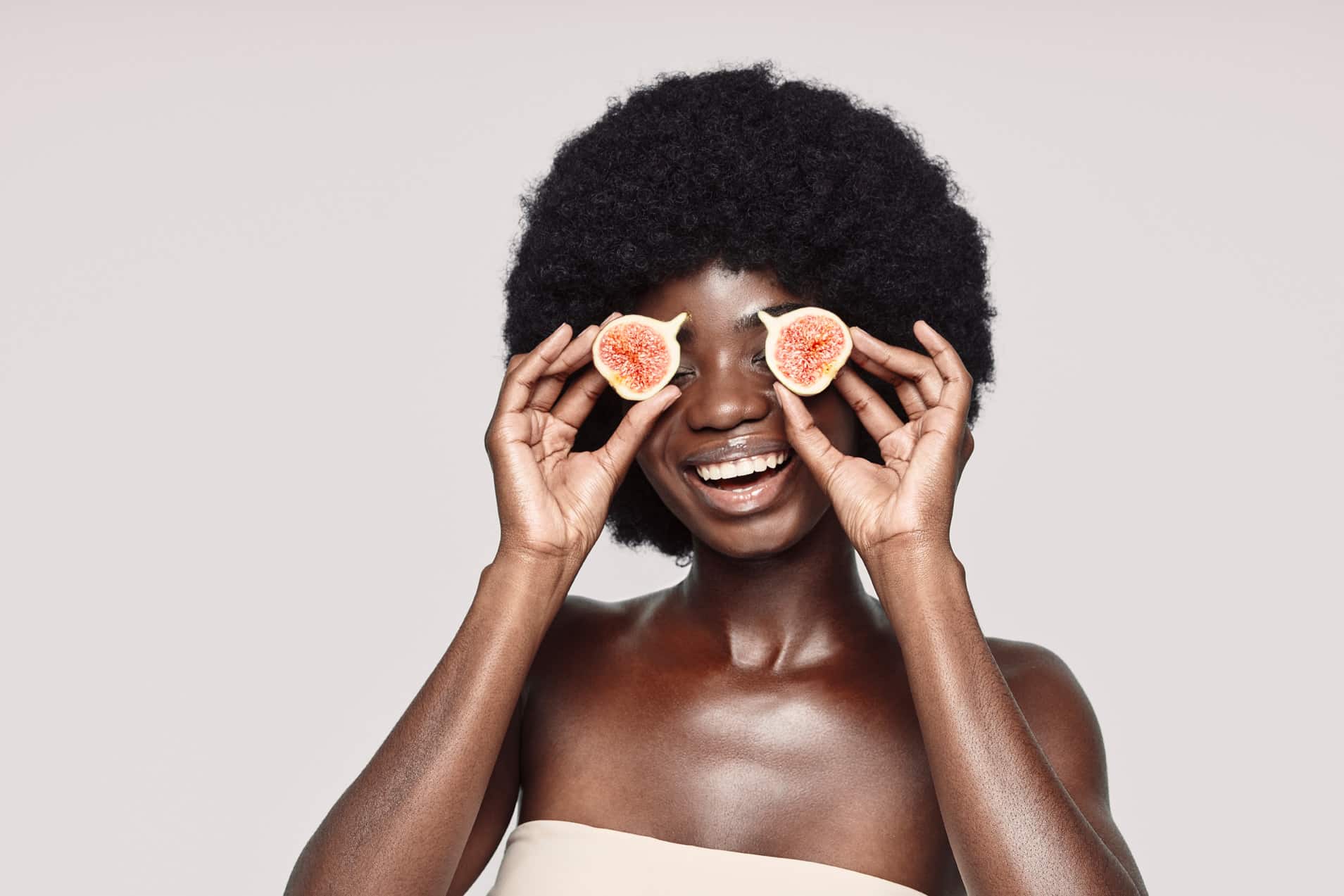 Portrait of beautiful young African woman covering eyes with fig slices and smiling