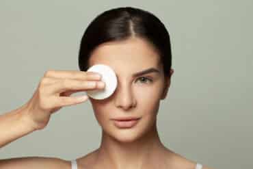 Beautiful woman with flawless skin is holding cotton pad on hand near her eyes