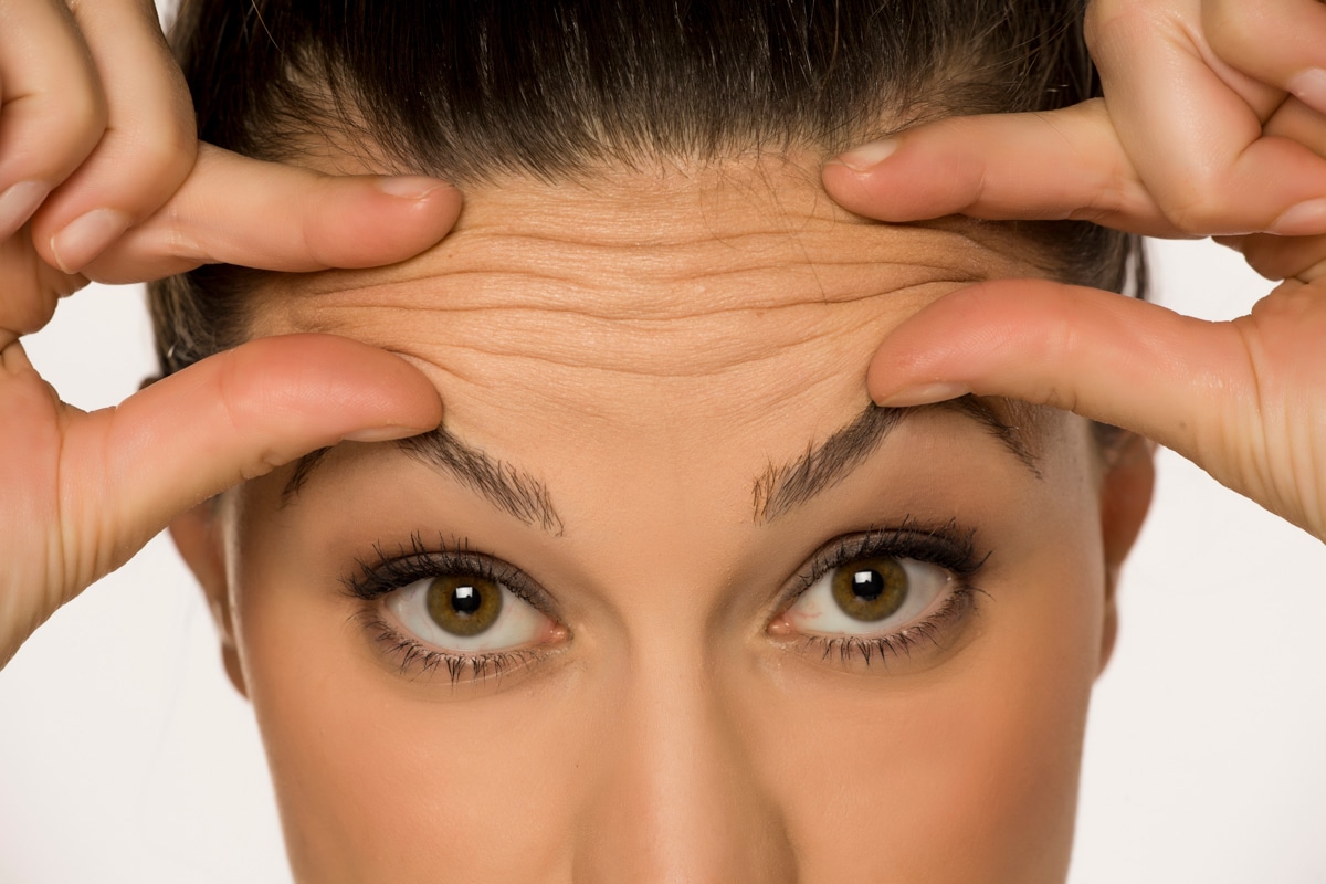 A woman pinches her forehead skin into wrinkles
