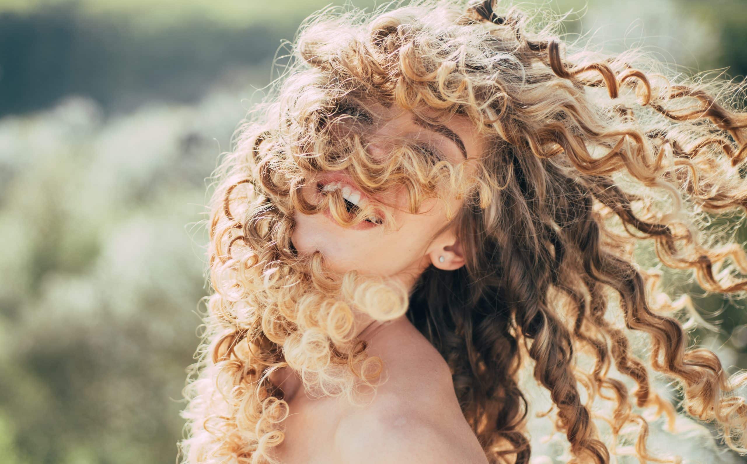 Blonde spring girl with curly beautiful hair smiling.